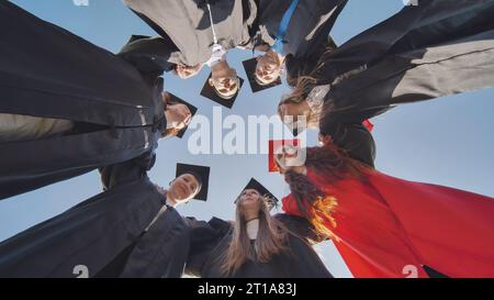 College graduates in a circle stand hugging each other. Stock Photo