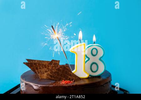 Number 18 birthday candle burning on cake, sparkler sparks fly. The eighteenth birthday or anniversary celebration concept. Lot of copy space on blue Stock Photo