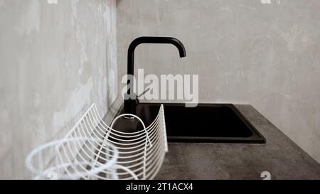 Close-up of a modern kitchen faucet and sink. Black tap on the sink. Farmhouse kitchen sink detail with black faucet. Faucet and sink in the kitchen. Stock Photo