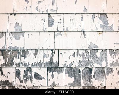 Close up texture detail showing peeling white paint against faded gray siding on old building in New England. Stock Photo