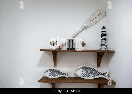 decorative fish, lighthouse and plants against white wall on wooden shelves form nautical seaside display Stock Photo