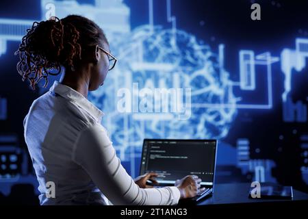 African american engineer updating AI systems, writing intricate binary code scripts on laptop. Tech support using programming to upgrade artificial intelligence simulation model Stock Photo