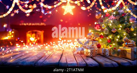 Present Below Christmas Tree With Garlands In Home Interior With Fireplace And Star - Abstract Defocused Lights Stock Photo