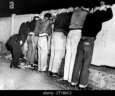 Seven men line up on fence as they are frisked by a policeman, Pacific St. between Carlton and Vanderbilt Avenues, Brooklyn, New York City, New York, USA, Orlando Fernandez, New York World-Telegram and the Sun Newspaper Photograph Collection, 1956 Stock Photo
