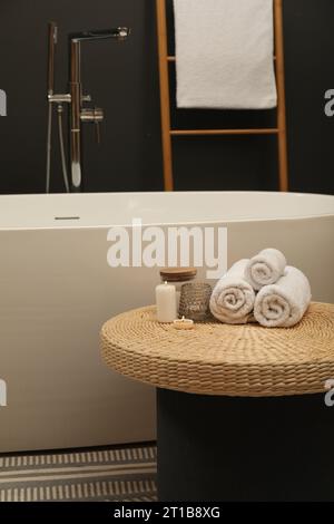 Spa day. Towels and candles on wicker table near tub in bathroom Stock Photo