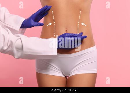Doctor and patient preparing for cosmetic surgery, pink background. Woman with markings on her abdomen, closeup Stock Photo
