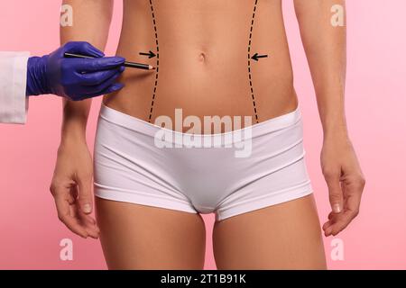 Woman preparing for cosmetic surgery, pink background. Doctor drawing markings on her abdomen, closeup Stock Photo