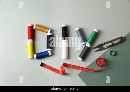 Abbreviation DIY made of spools of colorful threads and sewing supplies on color background, flat lay Stock Photo