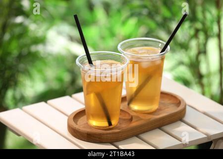 Plastic cups of tasty iced tea with lemon on white wooden table against blurred background Stock Photo
