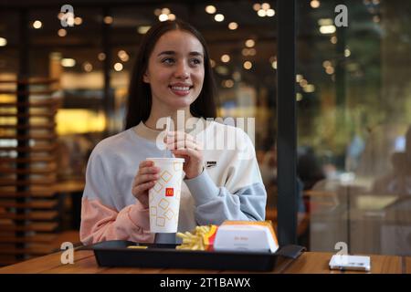 Lviv, Ukraine - September 26, 2023: Woman with McDonald's drink, burger and french fries at table in restaurant Stock Photo