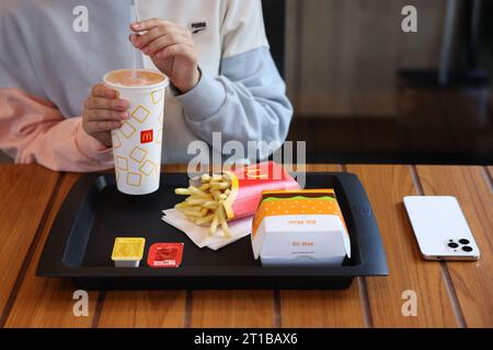 Lviv, Ukraine - September 26, 2023: Woman with McDonald's drink, burger and french fries at wooden table in restaurant, closeup Stock Photo