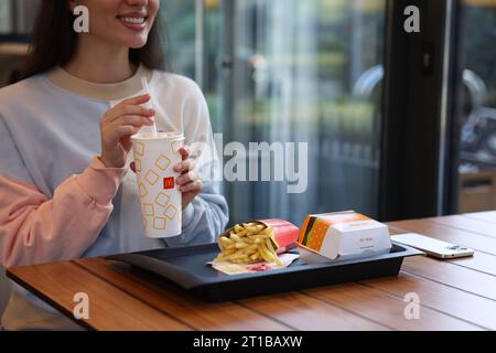 Lviv, Ukraine - September 26, 2023: Woman with McDonald's drink, burger and french fries at wooden table in restaurant, closeup Stock Photo