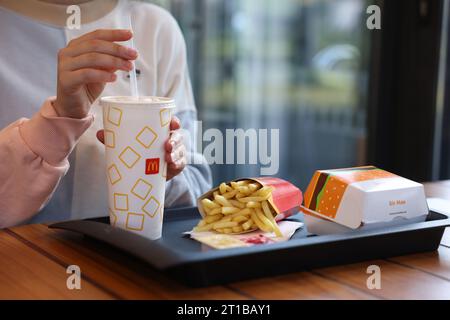 Lviv, Ukraine - September 26, 2023: Woman with McDonald's drink, burger and french fries at wooden table in restaurant, closeup Stock Photo