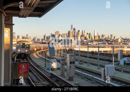 Golden hour view of New York City skyline and an approaching G train at Sunrise on the elevated railroad portion of the G line at Smith Street. Stock Photo