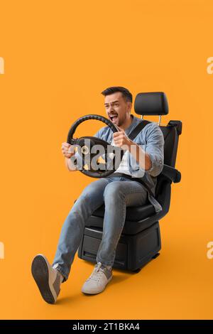 Handsome man with steering wheel shouting in car seat on yellow background Stock Photo