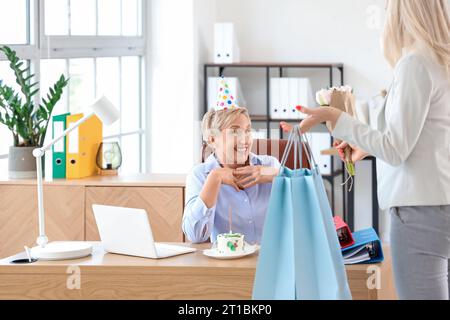 Mature woman receiving bags with birthday gifts in kitchen Stock Photo ...