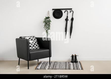 Stylish armchair, shoes and umbrellas hanging on light wall Stock Photo