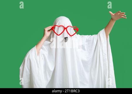 Woman in Halloween costume of ghost and funny glasses on green background Stock Photo