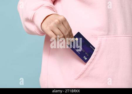 Young woman putting credit card into pocket on blue background, closeup Stock Photo