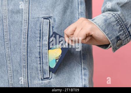 Young woman putting credit card into pocket on pink background, closeup Stock Photo