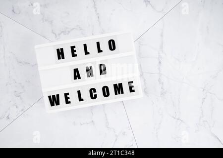Hello and welcome written white lightbox sitting on white marble background. Stock Photo