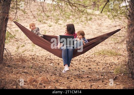 Working away from office concept, man working on laptop while lying in hammock in a forest, focus on monitor. Stock Photo