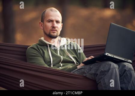 Man Hiker Working on laptop in Hammock in pine forest. Remote working concept. Stock Photo