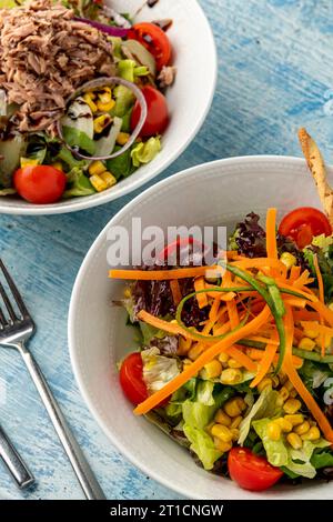 Salad with tuna, carrots, tomatoes, corn and plenty of greens on white porcelain plates Stock Photo
