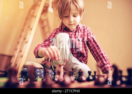 Cute preschool boy are playing chess at home. Funny face, selective focus. Stock Photo