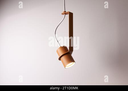 Glowing metal orange lamp is hanging on the cable on the gray background. Closeup photo. No people. Stock Photo