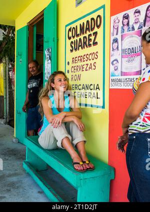 A young woman sits on a bench outside a bar and speaks with the local contingent from this small town in Puerto Rico. Stock Photo