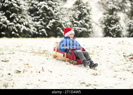 Boy wearing Santa hat sledding down a hill in winter Stock Photo