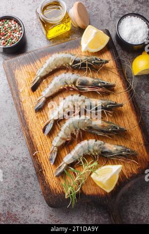 Raw tiger prawns with lemon spices, and herbs closeup on the wooden board on a dark grunge background. Vertical top view from above Stock Photo