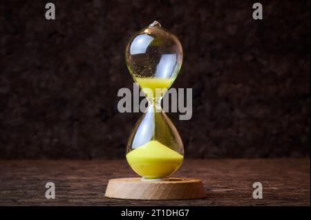 Sand running through the bulbs of an hourglass on a dark cork tree background close up. Stock Photo