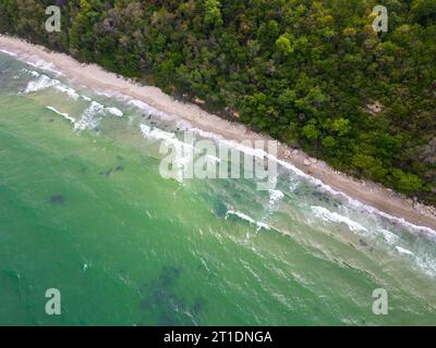 From above, the mesmerizing beach unfolded with golden sand caressed by turquoise waves. Lush green forests adorned the coastline, while sturdy rocks Stock Photo