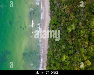 From above, the mesmerizing beach unfolded with golden sand caressed by turquoise waves. Lush green forests adorned the coastline, while sturdy rocks Stock Photo