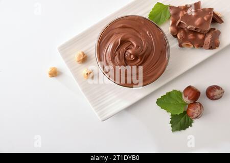 Cocoa cream with hazelnuts and portions of chocolate and nuts on a white plate isolated on a white table. Top view. Stock Photo