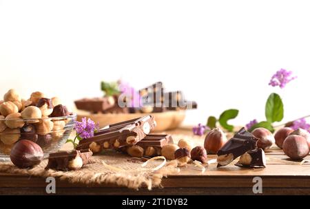 Detail of slices of chocolate with hazelnuts on wooden table with nuts isolated white. Front view. Stock Photo