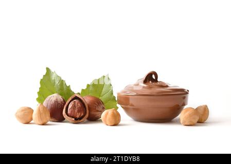 Hazelnuts and cocoa cream in glass bowl and leaves behind isolated on white. Front view. Stock Photo