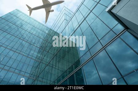 Airplane flying in the sky above modern sustainable glass office building. Exterior skyscraper green glass building. Business travel. Aviation Stock Photo