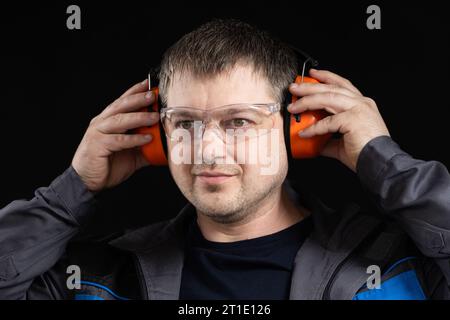 A man in earmuffs, glasses and overalls on a black background. Stock Photo