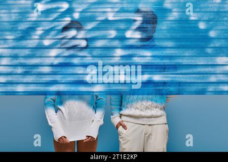 couple in white knitted sweaters behind blue frozen plastic sheet in studio, winter fashion concept Stock Photo