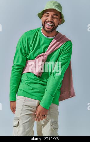cheerful young man in stylish outfit laughing sincerely on light blue backdrop, fashion concept Stock Photo