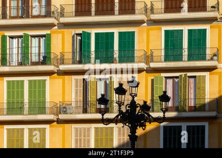 View of the yellow facades of old buildings with balconies and green wooden shutters in the Plaza Mayor of Palma (Mallorca, Spain) at sunset Stock Photo