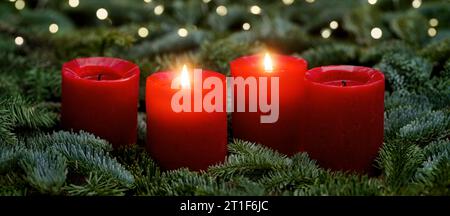 Red Advent candles, two burning, with fir branches and bokeh lights. The image is part of a set. Stock Photo