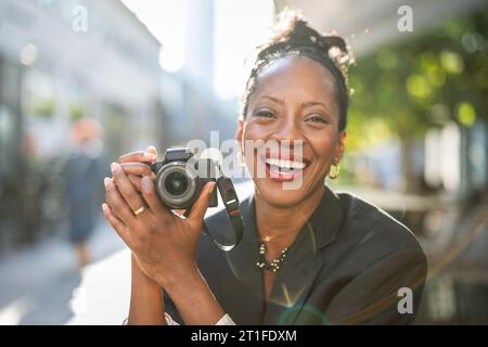 Portrait of smiling woman holding camera in the city Stock Photo