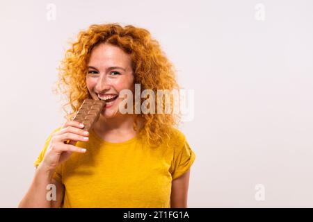 Portrait of happy cute ginger woman enjoys eating chocolate. Stock Photo