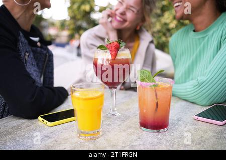 Close-up focus three colorful cocktail at table. Middle-aged multiracial women in background smiling Stock Photo