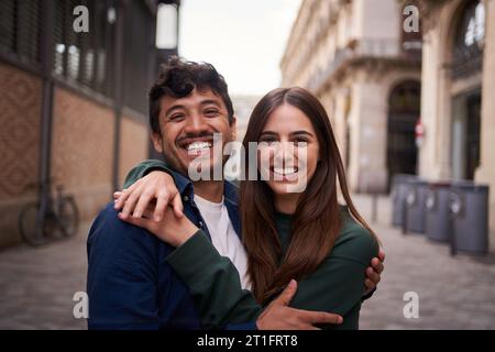 Portrait young multiracial couple embracing happy smiling face on street. Friends cheerful hugging. Stock Photo