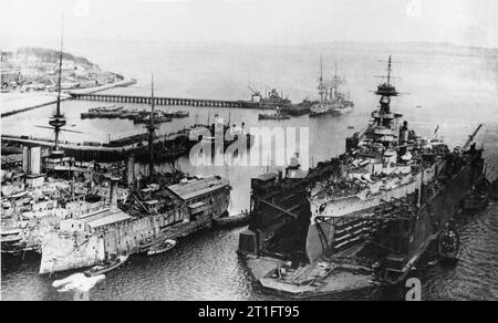 The British battleship HMS Erin in a floating dry dock, circa in 1918. The location may be Invergordon, Scotland (UK). In the left foreground are several old warships employed as barracks and for other stationary support duties. The one furthest right may be HMS Algiers (formerly HMS Triumph of 1873). That at the far left, with two smokestacks closely spaced side-by-side, may be HMS Mars of 1897. Stock Photo